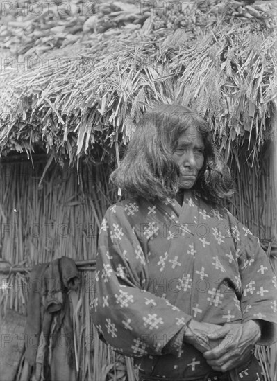 Ainu woman standing outside a hut, 1908. Creator: Arnold Genthe.