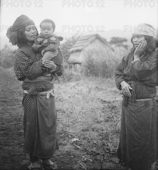 Two Ainu woman, one holding a child, standing outside, 1908. Creator: Arnold Genthe.