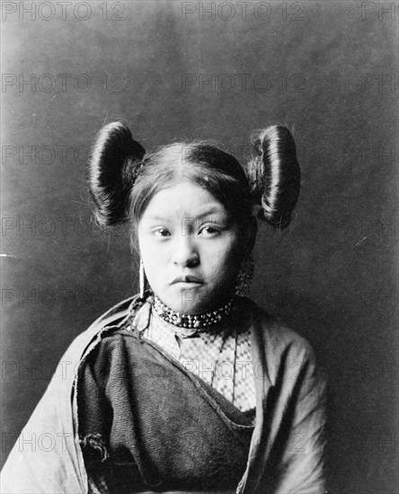 Gobuguoy, Walpi girl, half-length portrait, facing front, hair tied in swirls on sides of..., c1900. Creator: Edward Sheriff Curtis.
