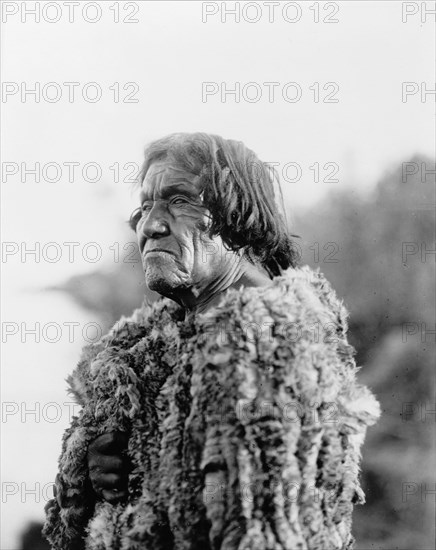 Mohave man, half-length portrait, facing left wearing "primitive" robe of rabbit skin, 1907. Creator: Edward Sheriff Curtis.