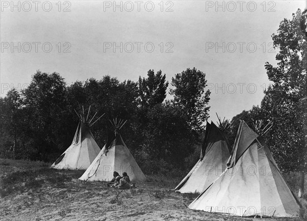 An Assiniboin camp containing four tepees with Indians seated on ground, c1908. Creator: Edward Sheriff Curtis.