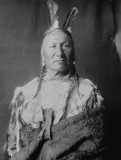 Yellow Horse-Yanktonai, half-length portrait, standing, facing slightly right, with long..., c1908. Creator: Edward Sheriff Curtis.