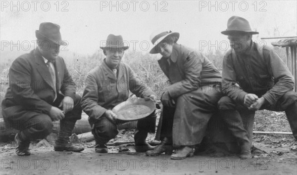 Group portrait of a woman and three men, crouched outside, smiling; one..., between c1900 and 1916. Creator: Unknown.