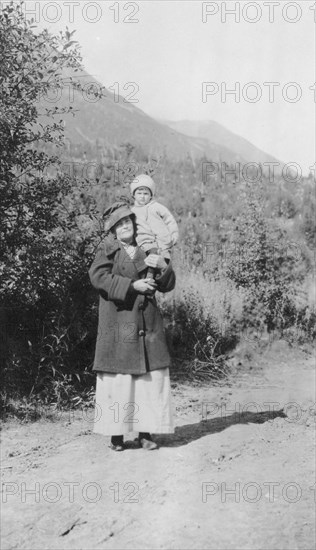 Woman standing on dirt road holding child; mountains in background, between c1900 and 1916. Creator: Unknown.