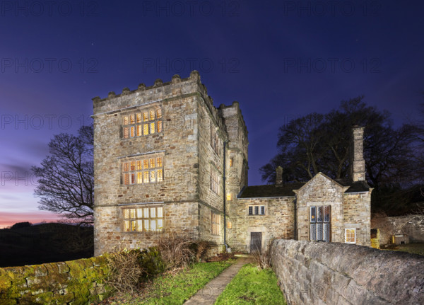 Exterior view, taken using a drone at sunset, showing North Lees Hall from the south-east with the windows illuminated, Hathersage, Outseats, Derbyshire, 2025. North Lees Hall is thought to have inspired Charlotte Bronte (1816-55) in the summer of 1845 when she was staying with her friend Ellen Nussey at the vicarage in Hathersage, providing the model for Mr Rochester's Thornfield Hall in her first and most famous novel Jane Eyre (1847).