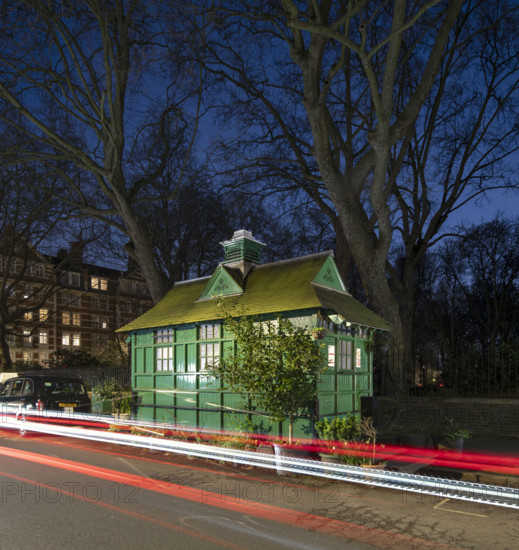 General view of the Cabmen's Shelter from the north-west, Wellington Place, St John's Wood, City of Westminster, London, 2024; showing car light trails at night.
