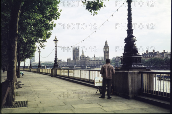 A man on the promenade on the south bank of the Thames near Hungerford Bridge, painting a picture of the view of the Houses of Parliament and Big Ben, London, 1983.