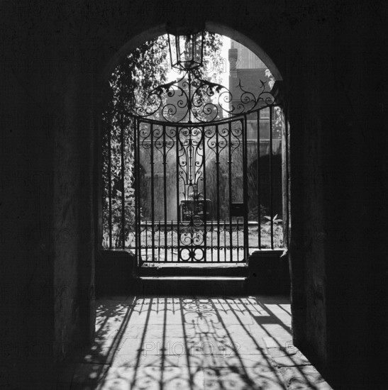 View looking through a decorative wrought iron gate in the Little Cloister at Westminster Abbey, London, 1946-1999; showing the fountain in the central courtyard.