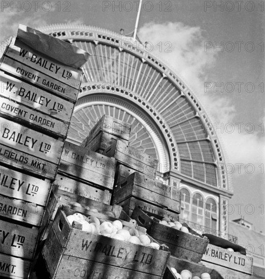 Looking up at the arched iron and glass facade of Covent Garden market's Floral Hall, with piles of fruit crates belonging to W. Bailey Ltd stacked in the foreground, London, 1945-1950. The Floral Hall is now part of the Royal Opera House.