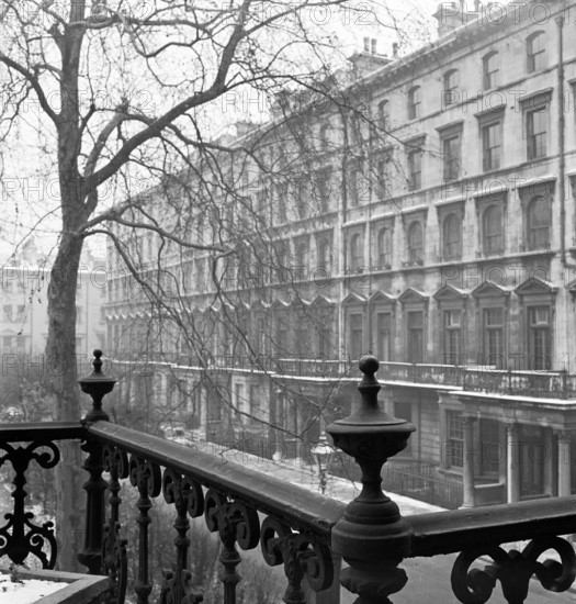 Looking along the side of a lightly-snowy London square from a raised position behind a wrought-iron rail, 1947.