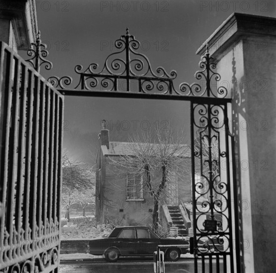 Detail of the wrought iron gate and overthrow at the Old Hall, Highgate, London, 1967; with the early 19th century cottages at numbers 23 to 25 South Grove visible in the background.
