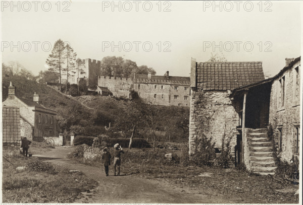 General view of Farleigh Hungerford Castle from the east, Norton St Philip, Mendip, Somerset, 1920-1950; with children in the foreground walking past two village houses below the castle.
