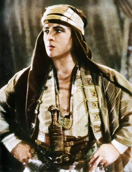 Rudolph Valentino in "The Sheik", 1921, (1935). Portrait of Rudolph Valentino (1895-1926), film actor born in Italy, one of the first 'Hollywood heartthrobs'. Valentino arrived in the United States in 1913 and found fame as a film star and sex symbol of the 1920s. When he died at the age of 31, of complications after surgery for appendicitis and gastric ulcers, 100,000 people lined the streets of Manhattan in New York to pay their respects at his funeral. From "The Silver Jubilee Book - The Story of 25 Eventful Years in Pictures". [Odhams Press Ltd., London, 1935], (Colorised black and white print).