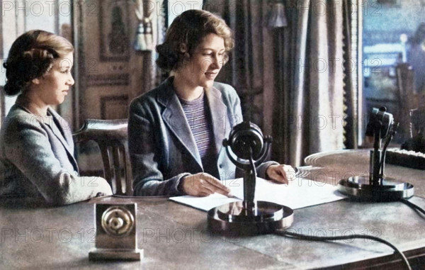'Broadcasting to the Children of the Empire - 13th October, 1940', 1947. Princess Elizabeth (future Queen Elizabeth II) and her younger sister Princess Margaret Rose at the microphone. From "Princess Elizabeth: The Illustrated Story of Twenty-one Years in the Life of the Heir Presumptive", by Dermot Morrah. [Odhams Press Limited, London, 1947]. (Colorised black and white print).