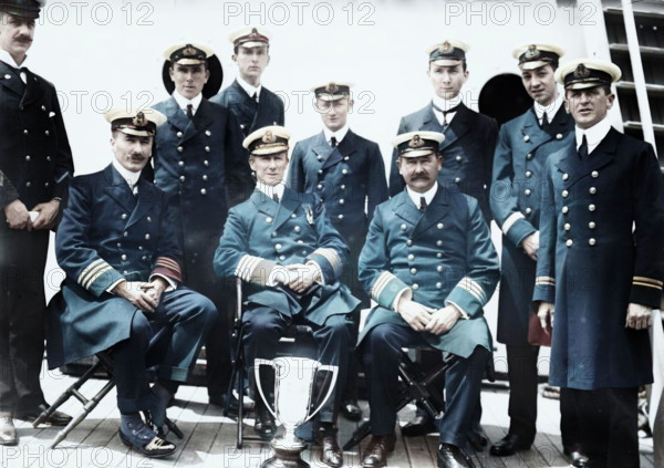 Captain Rostron & under officers of Carpathia [ship], 1912. Shows Captain Arthur Henry Rostron next to the silver loving cup presented to him in May 1912 by survivors of the Titanic in recognition of his heroism in their rescue. (Colorised black and white print).