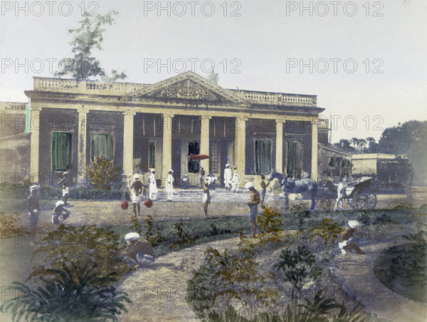 Residence of a European, India, 1850. Hand-coloured photograph showing a 'sahib' reclining on his veranda, while Indians tend to horses, carry water, and weed the garden.
