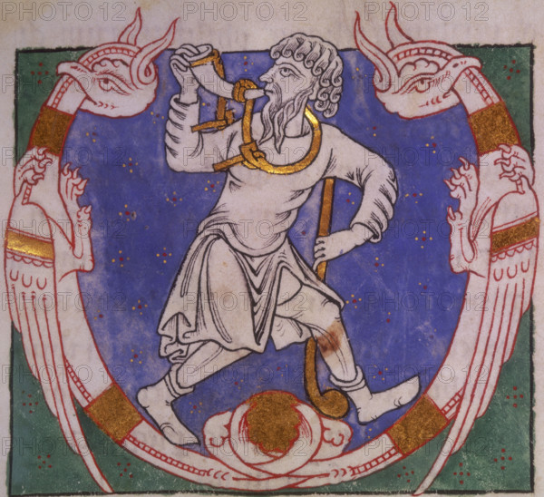 Amos, 1148. Beginning of the Book of Amos. Initial 'V', Amos blowing a horn, and carrying a club, between two winged creatures with entwined tails. From the Parc Abbey Bible.