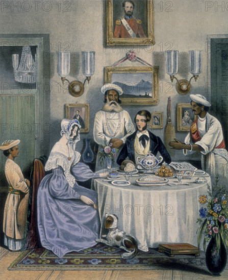 The Breakfast, 1842. A young married couple (an East India Company civil servant and his wife) breakfasting on fried fish, rice and Sylhet oranges, with servants in attendance. The lady of the house feeds titbits to a dog by her feet. The table is set with china, and family portraits hang on the wall. From "Sketches illustrating the manner and customs of the Indians and the Anglo-Indians".