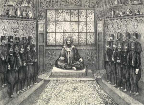 Audience of Hussein II Bey, 1835. Engraving showing Hussein II Bey (Al-Husayn II ibn Mahmud?) sitting cross-legged, surrounded by his Mamluk dignitaries in European-style uniform. Prince Hermann Ludwig Heinrich von Pückler-Muskau (1785-1871) was a German nobleman, renowned as an accomplished artist in landscape gardening, as well as the author of a number of books mainly centering around his travels in Europe and Northern Africa, published under the pen name of Semilasso. From "Atlas zu Semilasso in Afrika" by Prince Von Pueckler-Muskau).