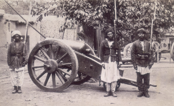 Three Afghan soldiers standing next to a cannon, Afghanistan, 1880s. Their rifles have bayonets fitted to them. Compared to the British Army their uniforms are very basic; military jackets over their normal clothes.