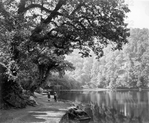 Lake at Naini Tal, India, c1865. Two people stand on the shore beside this picturesque, tree-lined lake. Naini Tal was a hill station in the Kumaon Hills of northern India.