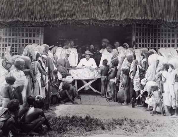 Paying wages to tea estate labourers, Bengal, 1880s. A European distributes pay to Indian workers, some of whom are young near-naked children.