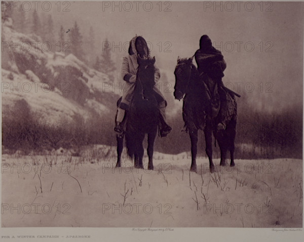 'For a Winter Campaign - Apsaroke', 1909. North American Indians on horseback. The warrior on the left wears the hooded overcoat of heavy blanket material that was generally adopted by the Apsaroke after the arrival of traders among them. The photograph was taken in a narrow valley among the Pryor mountains, Montana. From "The North American Indian: The complete Portfolios" by Edward S Curtis. [1909].