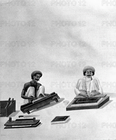 Two Indian bookbinders: one trimming page edges in a press, the other decorating a binding. Creator: Unknown.