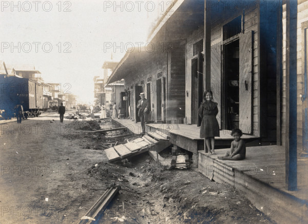 Colón, Panama: unpaved street lined with wooden houses; two children watch from a porch..., 1906. Creator: Unknown.
