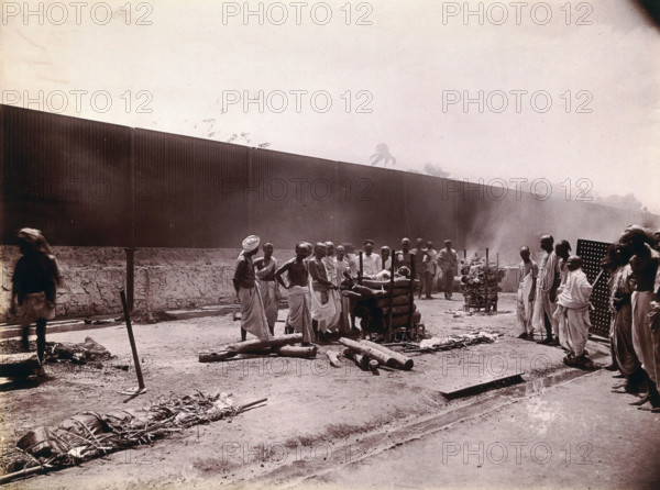A group of men stand around the body of a man laid out on a pyre of logs during a Hindu..., 1896/97 Creator: Unknown.