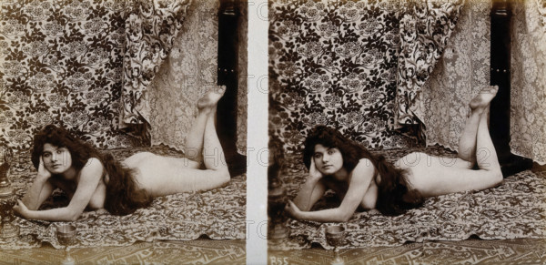 A young woman posing naked in a photographic studio, lying on her front on a piece of..., c1900. Creator: Unknown.