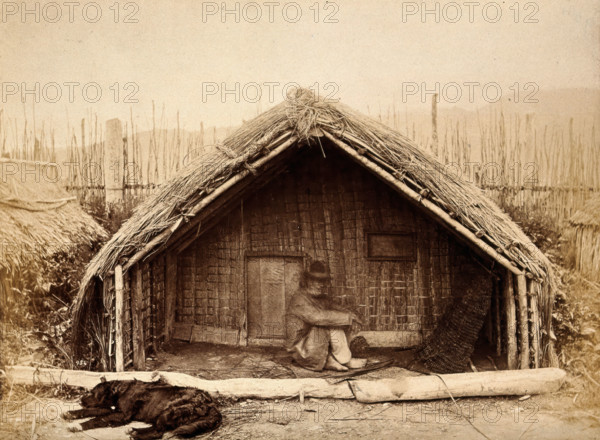 New Zealand: a Maori man sitting in front of a traditional house, between 1800 and 1899. Creator: Unknown.