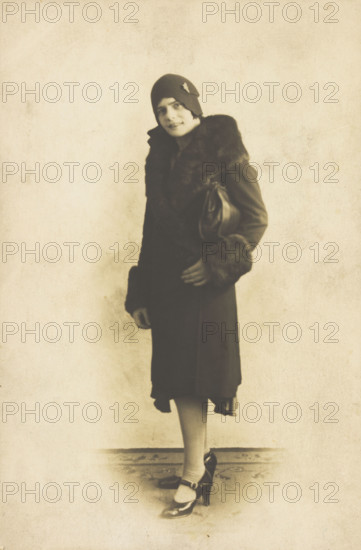A person poses wearing a long coat with fur trim and a hat with a brooch, [between 1920 and 1929?]. Creator: Unknown.