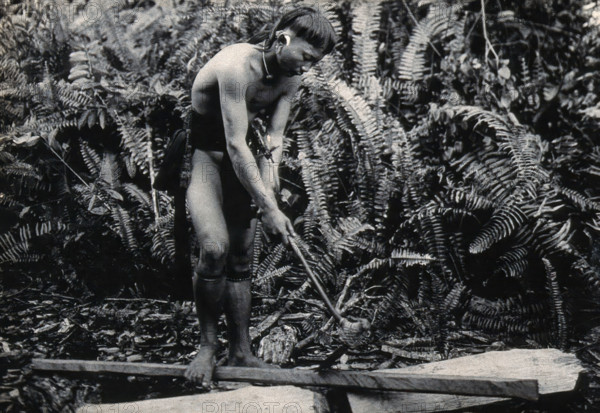 Sarawak: a Kenyah worker cutting a blowpipe from a block of wood, c1900. Creator: Unknown.