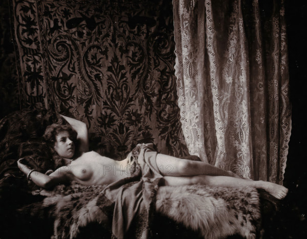 A young woman, posing semi-naked in a photographic studio, lying full-length on a fur..., c1900. Creator: Unknown.