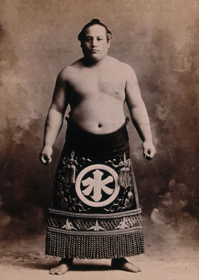 A young sumo wrestler posing in a photographic studio, wearing a richly decorated apron..., c1900. Creator: Unknown.