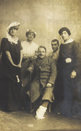 Four soldiers posing, three in drag, with an injured soldier seated in the centre, [1910-1919?]. Creator: Unknown.