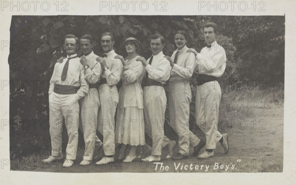 Entertainers, one in drag, pose in a line in front of foliage, [between 1910 and 1919?]. Creator: Unknown.
