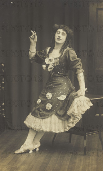 A performer in drag, wearing a large flowery dress, poses with a cigarette on stage, c1908-1910. Creator: Unknown.