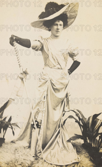 An man in drag is wearing a revealing dress and holding a staff, posing with his..., 1909. Creator: Unknown.