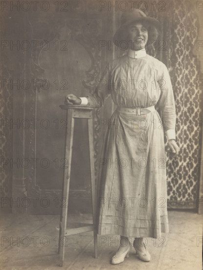 A sailor in drag leans on a high stool, in front of patterned scenery, (between 1910 and 1919?). Creator: Unknown.