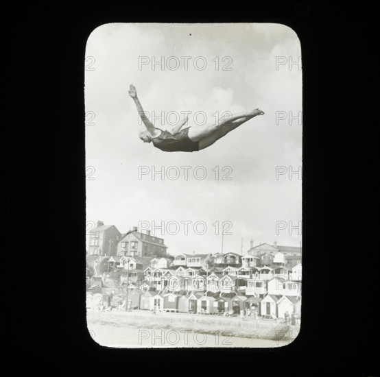 A swimmer diving into the sea at Southcliff, Walton-on-the-Naze, with beach huts on South..., 1920s. Creator: Norman Kingsley Harrison.