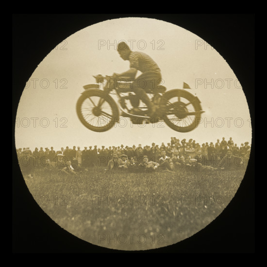 A view of a motorcycle jumping in front of a crowd of onlookers at an unknown..., 1920s-1930s.  Creator: Norman Kingsley Harrison.
