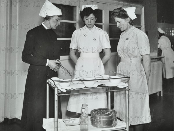 A Sister imparts knowledge and technical expertise to two trainee nurses, c1950s. Creator: Unknown.