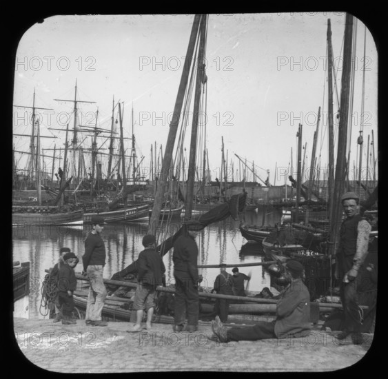 Men and boys with sailing boats in port, unknown location, c1900s. Creator: Robert Augustus Henry L'Estrange.