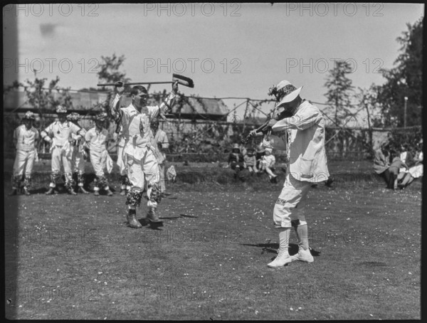 Bampton Morris troupe performing with a fiddler and someone holding a broom aloft, Oxon, 1920-30. Creator: George R Long.