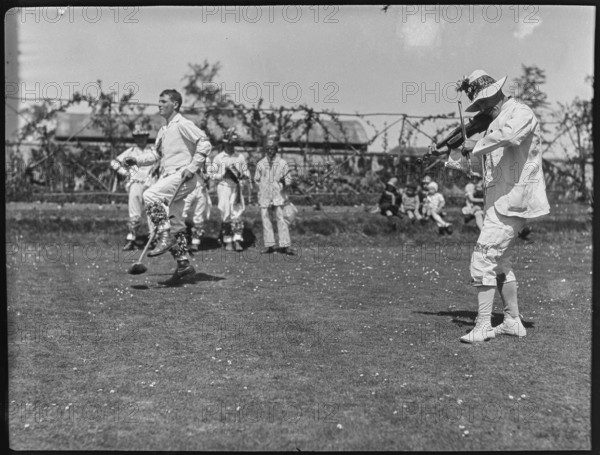 Bampton Morris troupe performing with a fiddler and someone holding a broom aloft, Oxon, 1920-30. Creator: George R Long.