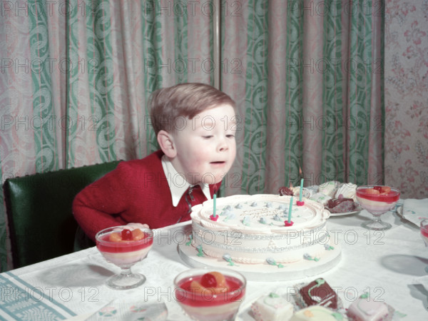 Birthday boy blowing out the candles on his cake, c1955.  Creator: Arthur Charles Kirby Ware.