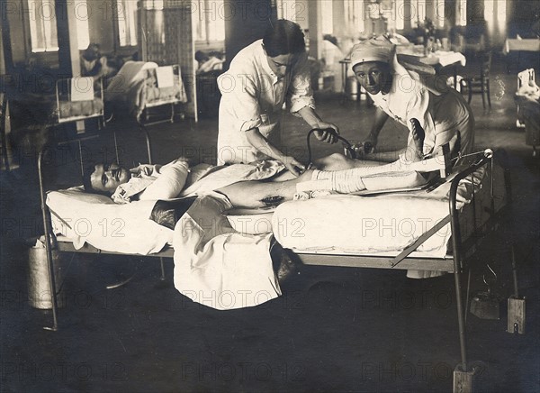 Dans un hôpital militaire à l'arrière du front, un médecin avec l'aide d'une infirmière, donnent des soins à un soldat blessé à une jambe - La première guerre mondiale 1914-1918.