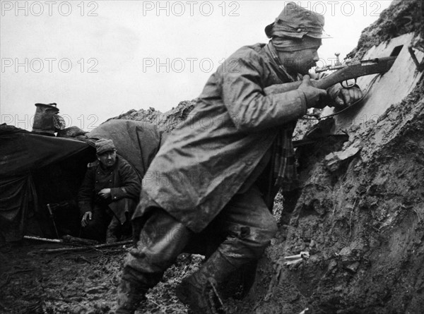 SOLDAT FRANCAIS DANS LA BOUE DES TRANCHEES DU NORD - En janvier 1915, dans une tranchée du Nord de la France, un soldat pointe son arme vers l'adversaire. A l'arrière plan, un abri creusé dans la terre est recouvert d'une toile de tente. Première Guerre Mondiale - Nous contacter pour la légende complète